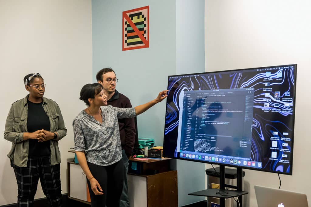 Trois personnes à côté d'un ordinateurs dans une salle de l'école Ada Tech School.